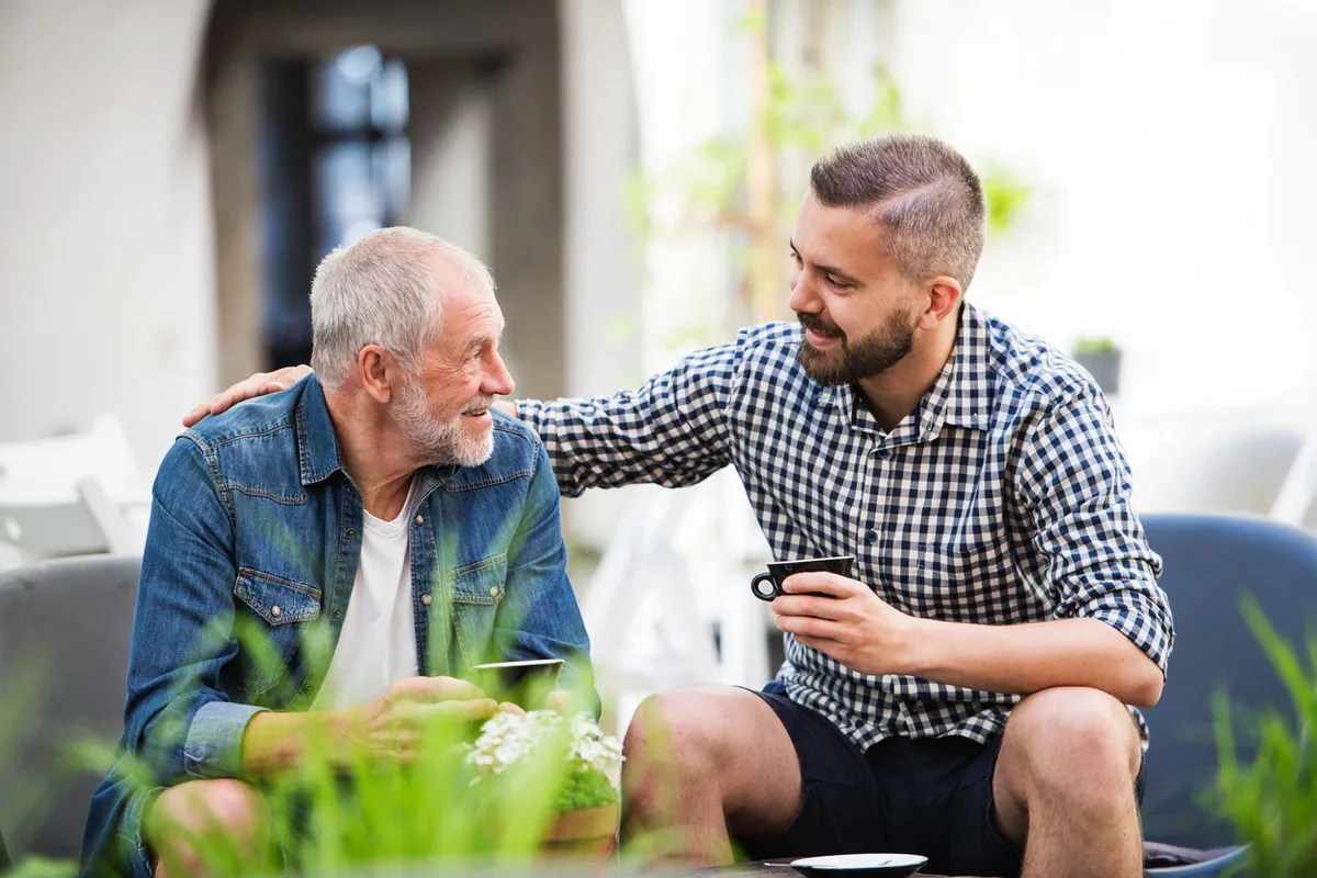 Talking to Parents About Assisted Living – Farmington Square Gresham Adult son talks with his father over coffee outdoors, discussing assisted living options at Farmington Square Gresham.
